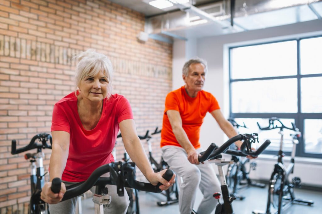 casal de idosos fazendo exercicos na bicicleta ergometrica numa academia.