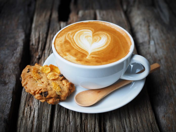 uma xicara de café com uma figura no creme, acompanhada de bbiscoitos.