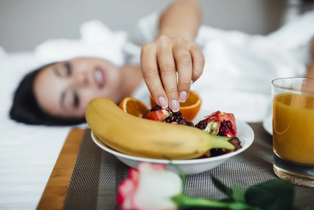 close do rosta de uma jovem, deitada, se servindo em um prato de frutas.