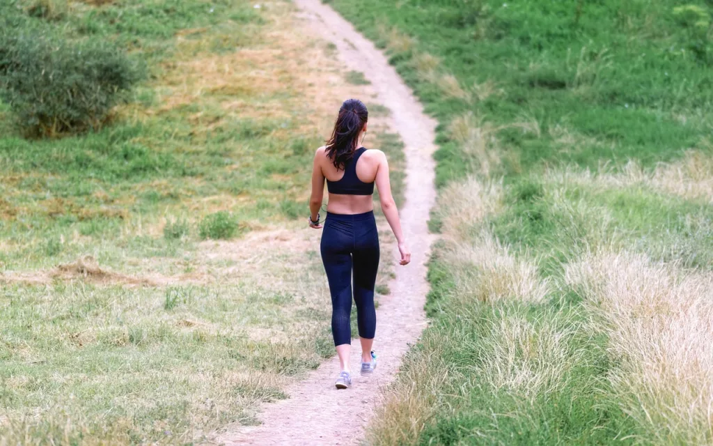 mulher com trajes de ginastica fazendo caminhada em paisagem aberta.