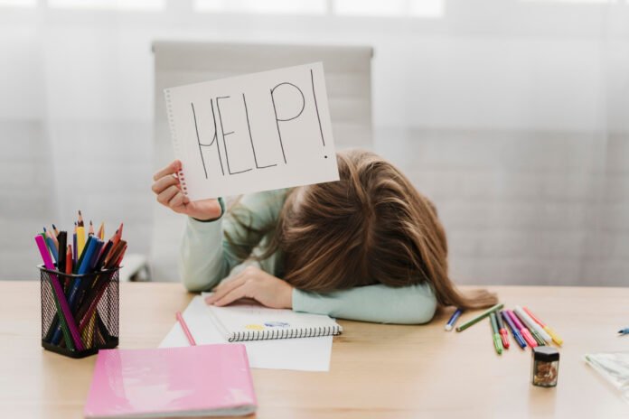 uma menina na sala de aula com a cabeça baixa, apoiada no braço e mostrando uma folha escrito help.