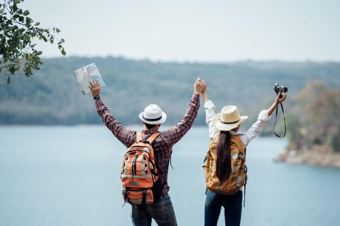 um casal visto de costas em roupas de viagem, segurando maquina fotografica e mapa.