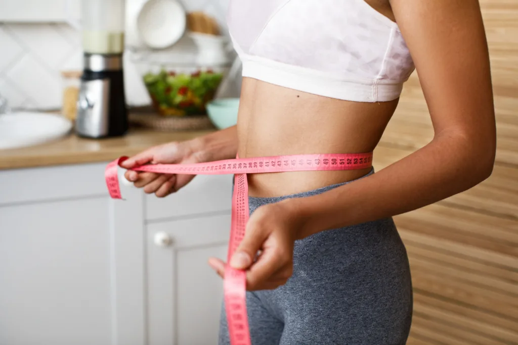 JOVEM ESBELTA MEDIDO O ABDOMEN COM UMA FITA METRICA.