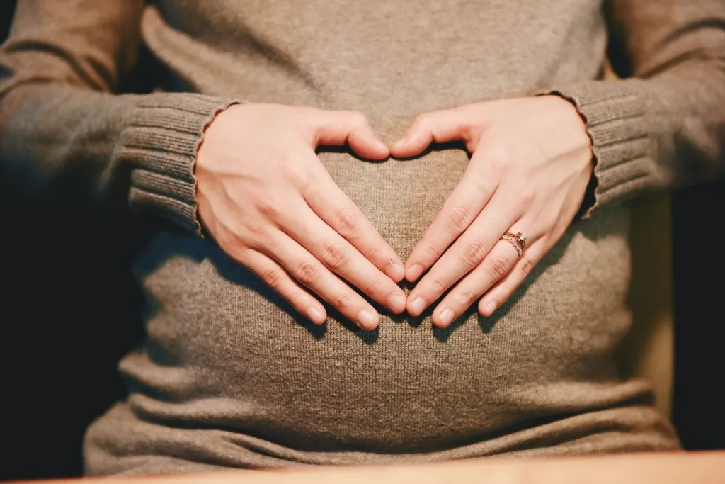 gravida fazendo o símbolo do coração sobre a sua barriga.
